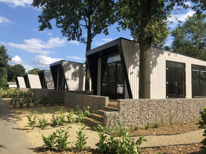 Moderna cabaña Just Nature en Limburg, Países Bajos, rodeada de vegetación y muros de piedra al sol.