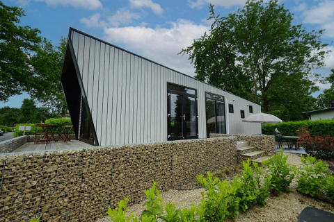 Moderno lodge Just Nature a Limburg, Paesi Bassi, con muro di pietra, terrazza e verde rigoglioso.