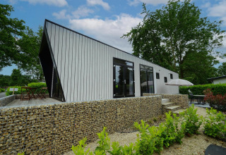 Lodge moderno Just Nature en Limburg, Países Bajos, con muro de piedra, terraza y vegetación.