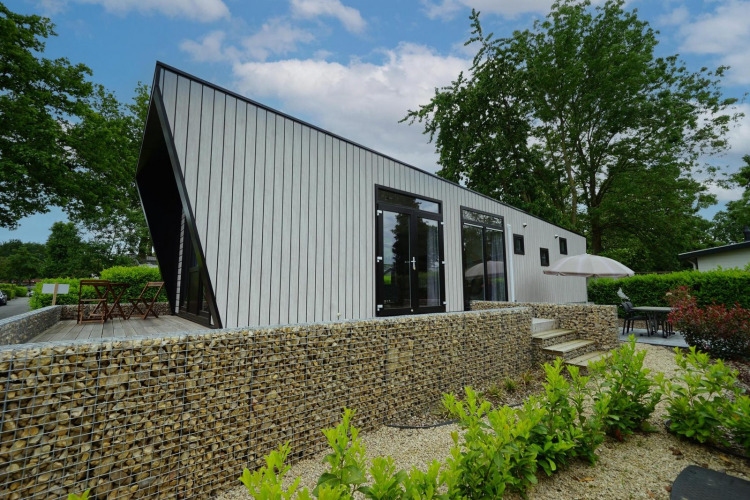 Lodge moderno Just Nature en Limburg, Países Bajos, con muro de piedra, terraza y vegetación.