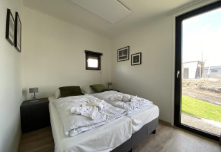 Dormitorio moderno en la cabaña Just Nature Light en Limburg, Países Bajos, con gran ventanal y decoración minimalista.