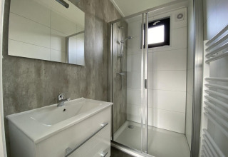Baño moderno en la cabaña Just Nature Light en Limburgo, Países Bajos, con ducha y tocador blanco.