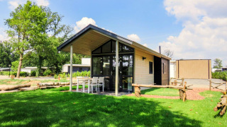 Foto van Tiny House-lodge met overdekt terras, buitentafel en stoelen op een groen grasveld.