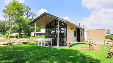 Foto van Tiny House-lodge met overdekt terras, buitentafel en stoelen op een groen grasveld.
