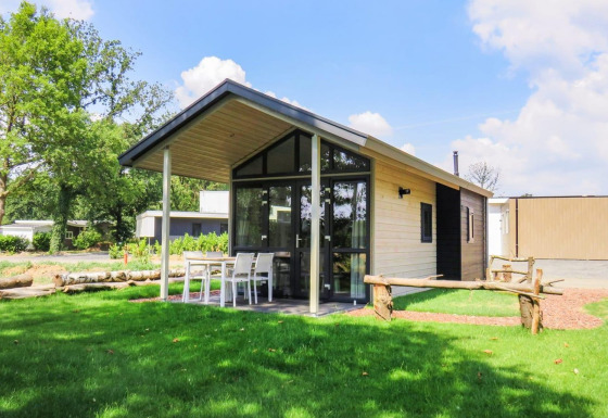 Foto van Tiny House-lodge met overdekt terras, buitentafel en stoelen op een groen grasveld.