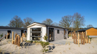 Lodge Berkel 4 moderne sur terrain sablonneux avec clôture en bois, arbres et ciel bleu dégagé.