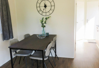 Eethoek in de Berkel 4-lodge aan Zuiderzee, Nederland, met tafel, stoelen en grote klok aan de muur.
