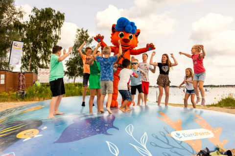 Kinder spielen und springen mit einem Maskottchen auf einem Spielplatz an einem Glamping-See.