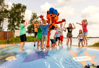 Kinder spielen und springen mit einem Maskottchen auf einem Spielplatz an einem Glamping-See.