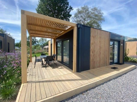 Moderne Domus 4 lodge met houten gevelbekleding, terras, pergola en tuinmeubilair in groene omgeving.
