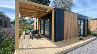 Moderne Domus 4 lodge met houten bekleding, terras, pergola en zitje in een groene omgeving.