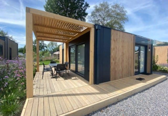 Moderne Domus 4 lodge met houten bekleding, terras, pergola en zitje in een groene omgeving.