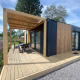 Moderne Domus 4 lodge met houten bekleding, terras, pergola en zitje in een groene omgeving.
