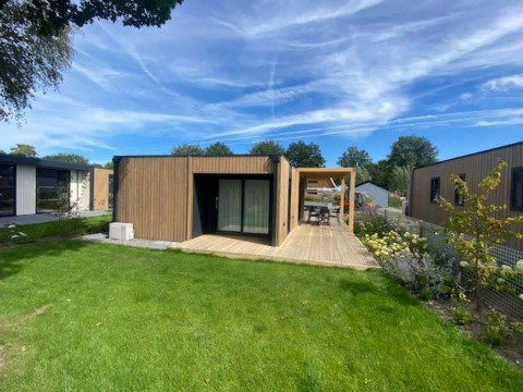Moderne lodge Domus 4 bij Zuiderzee in Nederland, omringd door groene tuin en blauwe lucht met wolken.