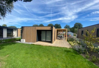 Moderna lodge Domus 4 a Zuiderzee, Paesi Bassi, circondata da prato verde e cielo azzurro con nuvole.
