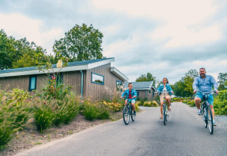 Familia paseando en bicicleta por un sendero en un glamping moderno con cabañas de madera y vegetación.