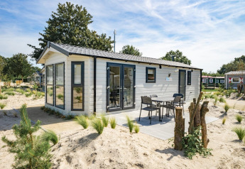 Moderne Berkel 6 Lodge mit Terrasse und Gartenmöbeln, umgeben von Sand und Pflanzen in Ferienanlage.