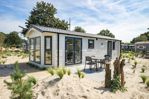 Modern Berkel 6 lodge with outdoor patio and furniture, surrounded by sand and greenery in a resort area.