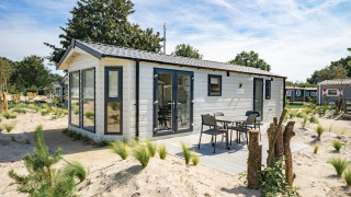 Modern Berkel 6 lodge with outdoor patio and furniture, surrounded by sand and greenery in a resort area.