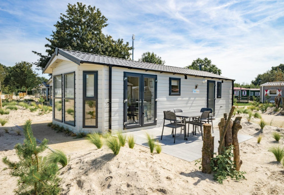 Modern Berkel 6 lodge with outdoor patio and furniture, surrounded by sand and greenery in a resort area.