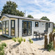 Moderne Berkel 6-lodge med terrasse og havemøbler, omgivet af sand og grønt i et afslappende ferieområde.