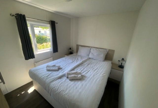 Lichte slaapkamer in de Berkel 6 lodge aan Zuiderzee, Nederland, met groot tweepersoonsbed en raam.