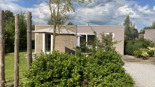 Vue extérieure du lodge Cosy Unique 2+4 au design moderne avec parasol et végétation luxuriante devant.