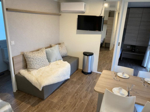 Moderne lodge zithoek met sofa, eettafel en TV bij Cosy Unique 2+4 in Zuiderzee, Nederland.