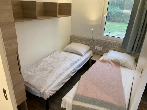 Twee enkele bedden in een kleine moderne kamer met raam in Cosy Unique 2+4 lodge bij Zuiderzee, Nederland.