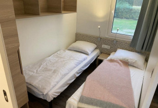 Twee enkele bedden in een kleine moderne kamer met raam in Cosy Unique 2+4 lodge bij Zuiderzee, Nederland.