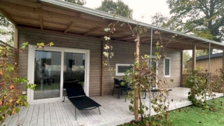 Terrasse en bois couverte du lodge Cosy Unique 4 avec transat, table et chaises, entourée de verdure.