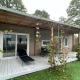 Udendørs terrasse ved Cosy Unique 4 lodge med liggestol, bord og stole under en overdækket veranda.