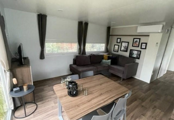 Wohnbereich der Cosy Unique 4-Lodge am Zuiderzee, Niederlande, mit Sofa, Esstisch und TV.