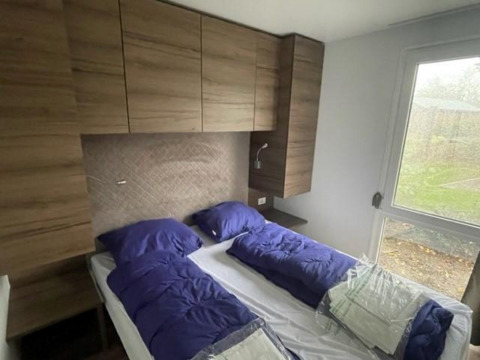 Slaapkamer in Cosy Unique 4 lodge aan Zuiderzee, Nederland, met twee bedden, houten kasten en groot raam.