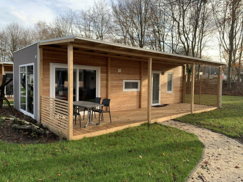 Billede af en moderne træhytte, Cottage 4, med overdækket terrasse og udendørs siddeplads i grønne omgivelser.