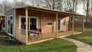Billede af en moderne træhytte, Cottage 4, med overdækket terrasse og udendørs siddeplads i grønne omgivelser.