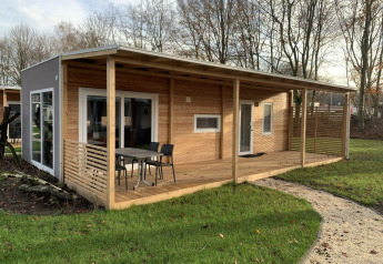 Billede af en moderne træhytte, Cottage 4, med overdækket terrasse og udendørs siddeplads i grønne omgivelser.