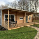 Billede af en moderne træhytte, Cottage 4, med overdækket terrasse og udendørs siddeplads i grønne omgivelser.