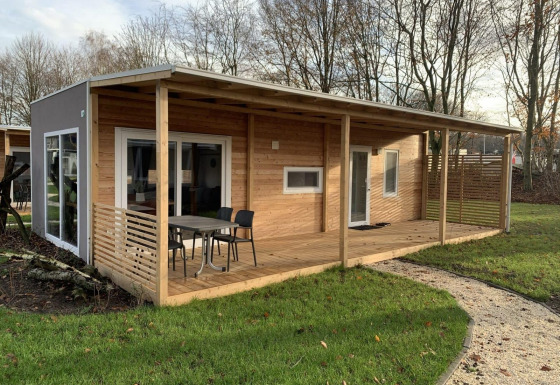 Billede af en moderne træhytte, Cottage 4, med overdækket terrasse og udendørs siddeplads i grønne omgivelser.
