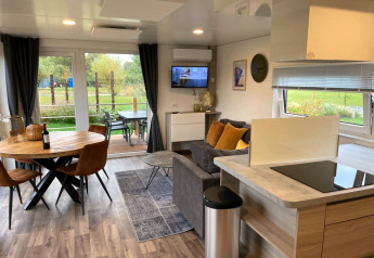 Soggiorno moderno al Cottage 4 di Zuiderzee, Paesi Bassi, con tavolo da pranzo, divano e vista sul verde.