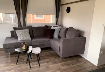 Soggiorno del Cottage 4 a Zuiderzee, Paesi Bassi, con divano grigio ad angolo, tavolini e cuscini.