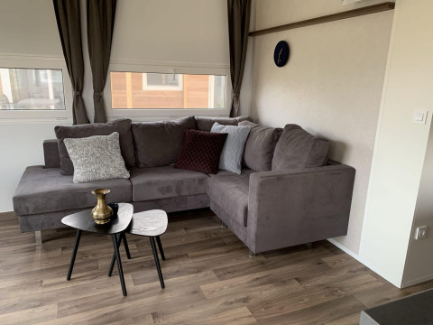 Sala de estar en Cottage 4 en Zuiderzee, Países Bajos, con sofá gris en esquina, mesas y cojines.