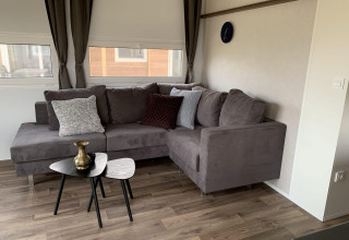 Sala de estar en Cottage 4 en Zuiderzee, Países Bajos, con sofá gris en esquina, mesas y cojines.