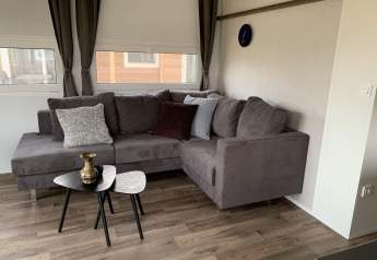 Woonkamer in Cottage 4 aan Zuiderzee, Nederland, met grijze hoekzetel, tafeltjes en sierkussens.