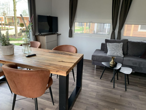 Salón moderno en Cottage 4, Zuiderzee, Países Bajos, con mesa de madera, sillas y cómodo sofá gris.