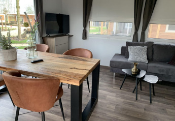 Salón moderno en Cottage 4, Zuiderzee, Países Bajos, con mesa de madera, sillas y cómodo sofá gris.