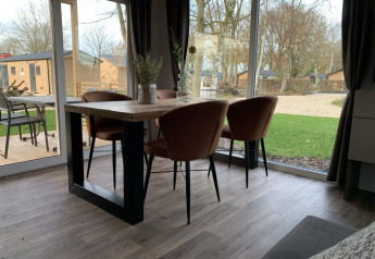 Eettafel met vier stoelen in een lodge met zicht op grasveld en bomen bij Zuiderzee, Nederland.