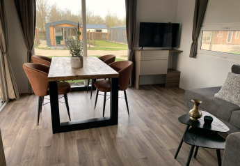 Sala moderna en Cottage 4 en Zuiderzee, Países Bajos, con mesa de comedor, sillas, televisor y amplias ventanas.