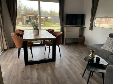 Sala moderna en Cottage 4 en Zuiderzee, Países Bajos, con mesa de comedor, sillas, televisor y amplias ventanas.