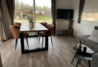 Moderne leefruimte in Cottage 4 op Zuiderzee, Nederland, met eettafel, stoelen, tv en grote ramen met zicht.